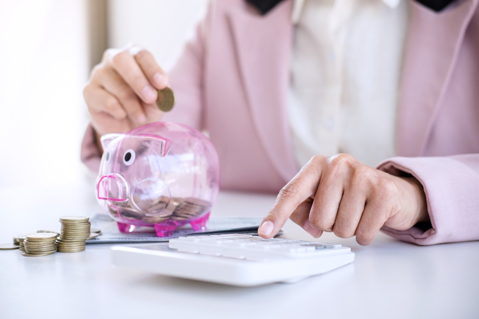 Business woman putting coins into piggy bank and using calculator to analysis business investment strategy with income of money coin and dollar, financial concept.