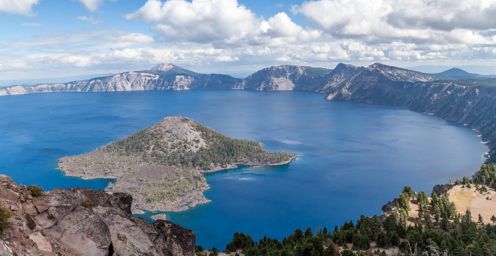 The deep blue Crater Lake and Wizard Island as seen from Watchman Peak Trail on the western rim opposite Mt. Scott in the Southern Oregon Cascades on a late summer day with clouds.