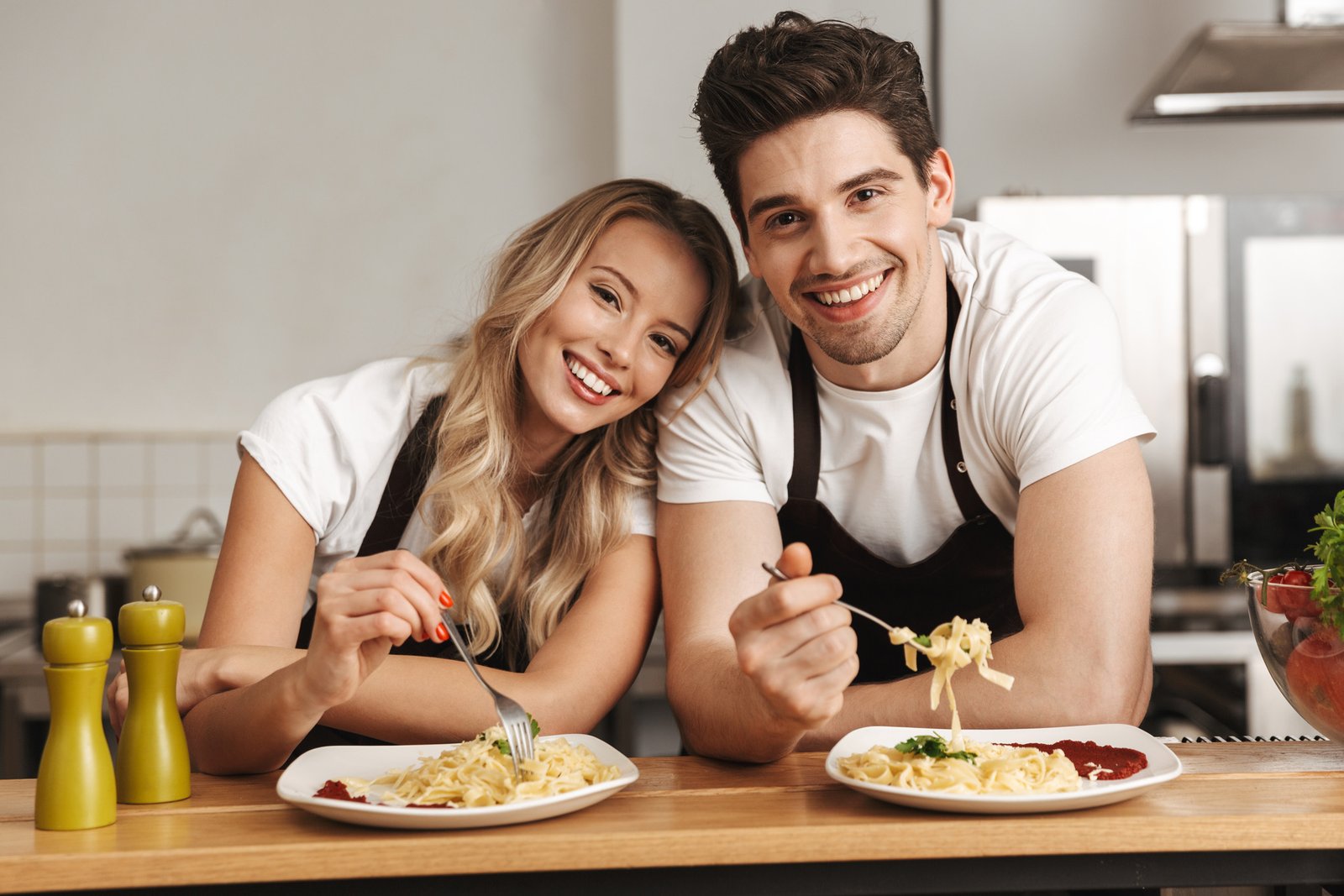 Image of happy excited young friends loving couple chefs on the kitchen eat tasty pasta.