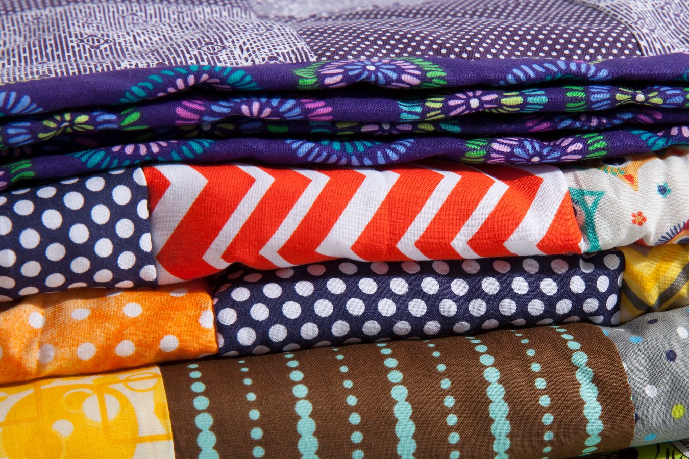 A close up of stacked quilts showing different patterns and cloth texture.