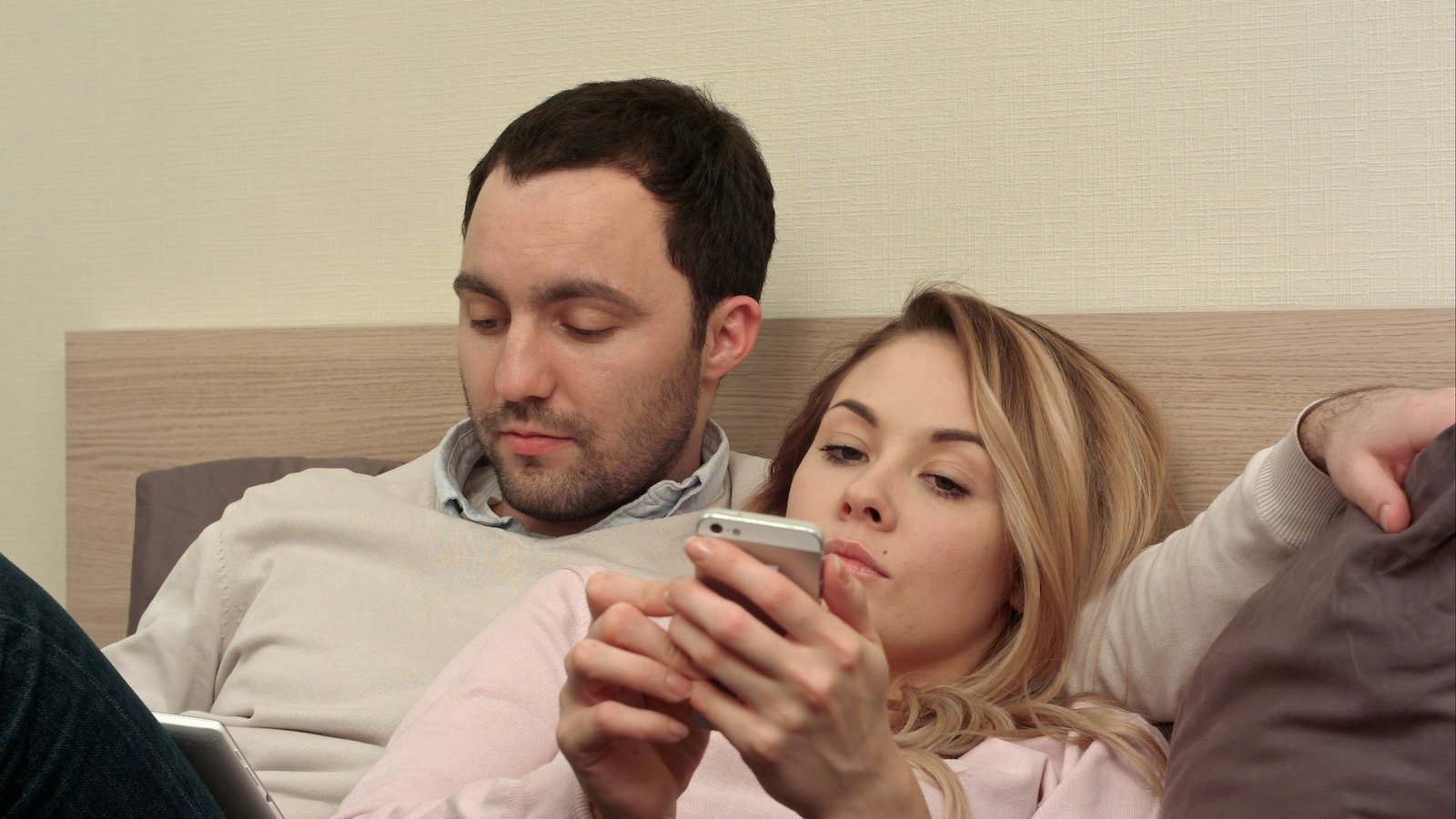 Young couple lying in bed, man using digital tablet, bored woman using smartphone. Close up. Professional shot in 4K resolution. 072. You can use it e.g. in your commercial video, business, presentation, broadcast video.