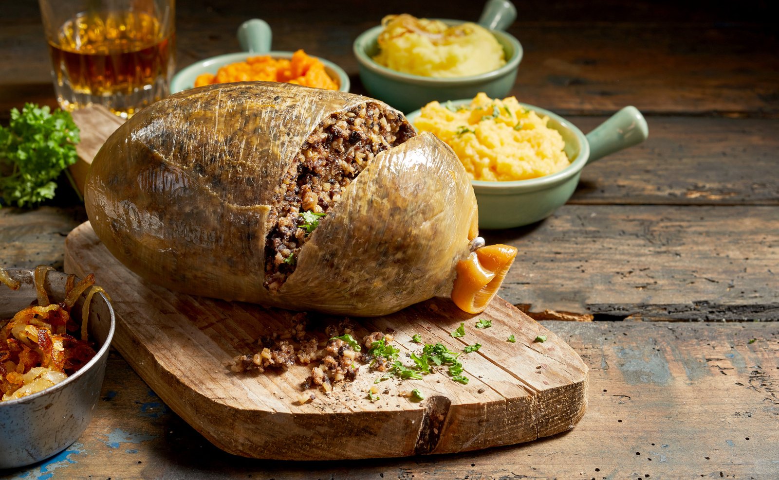 Cooked sliced open haggis and vegetables with mashed turnip, potato and fried onions on a rustic wood table with copy space