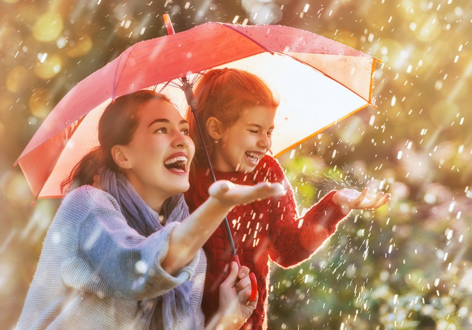 Happy funny family with red umbrella under the autumn shower. Girl and her mother are enjoying rainfall. Kid and mom are playing on the nature outdoors. Walk in the park.