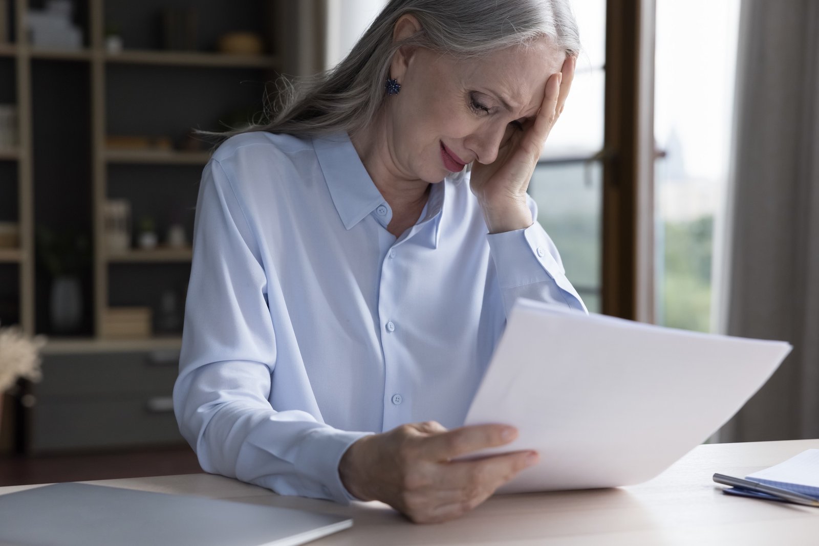 Unhappy sad senior grey haired business woman getting bad shocking news, reading document, paper letter, notification, crying. Elderly age problems, loss, stress concept