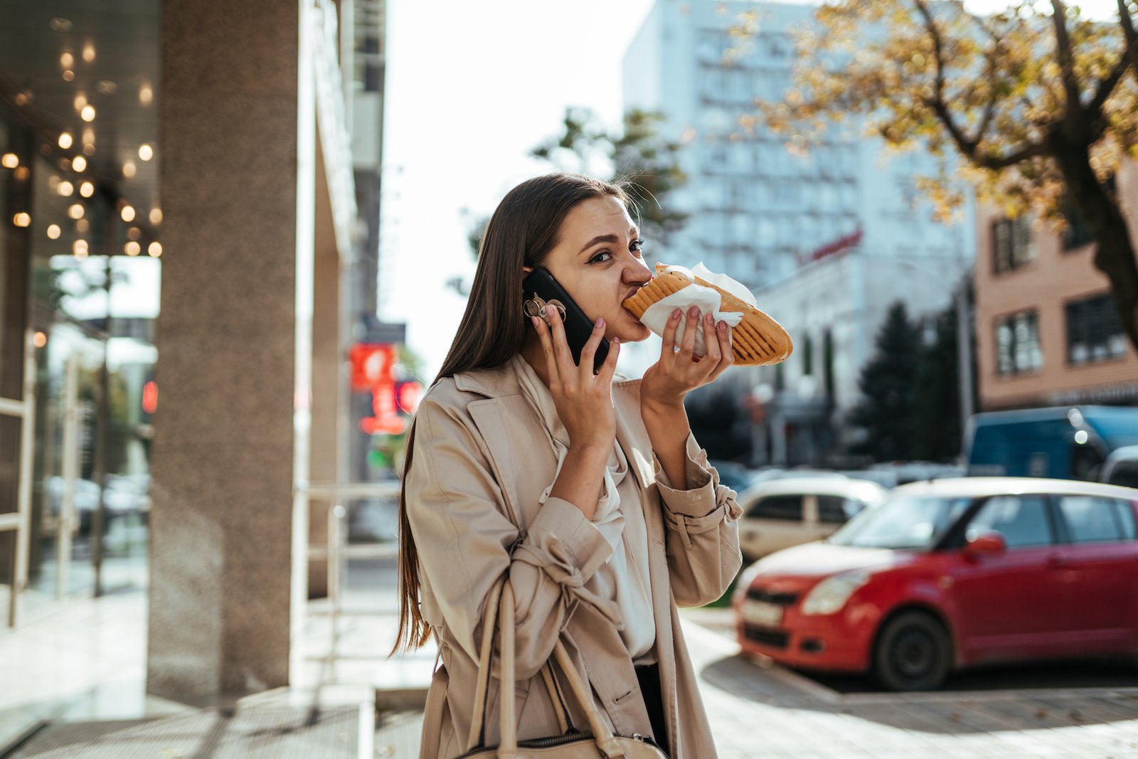 Stressed office woman eating on the way and talking on the phone outside